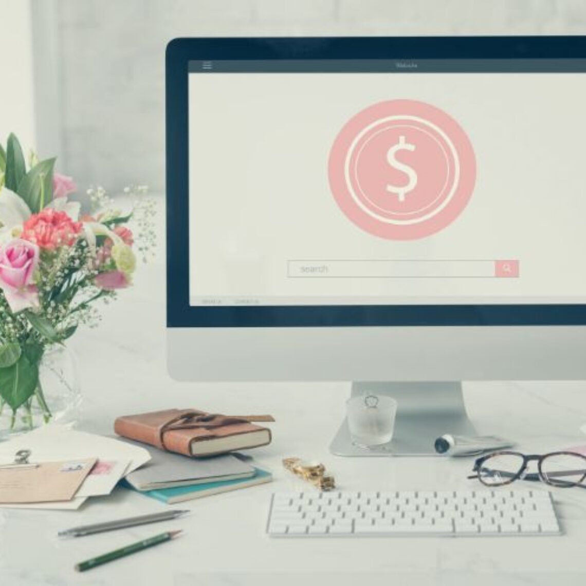 desktop mac computer with flowers to the left and a wireless keyboard that has a white screen and a light pink circle with a dollar sign in the middle.